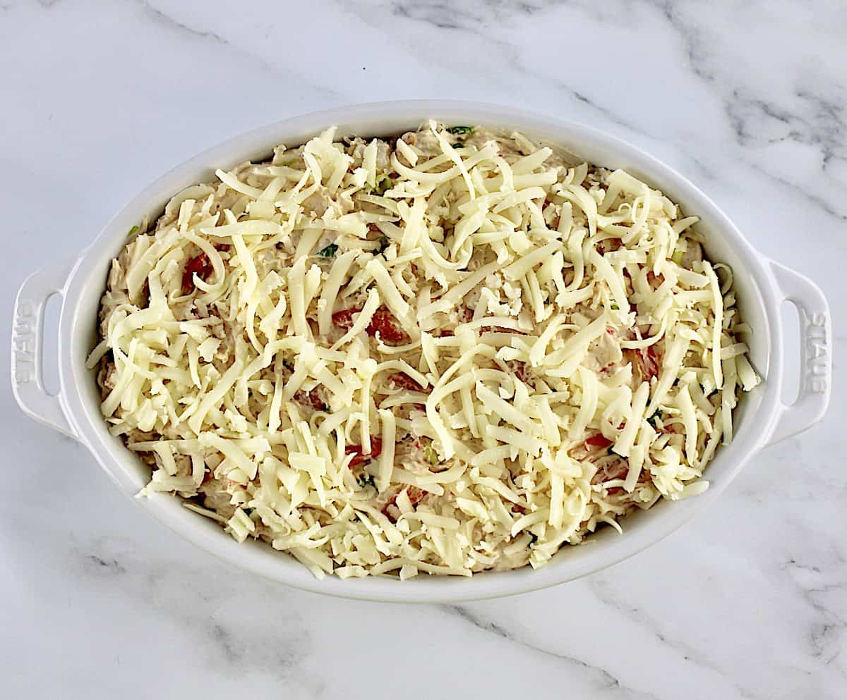 Hot Crab Dip in white oval casserole unbaked with shredded mozzarella cheese