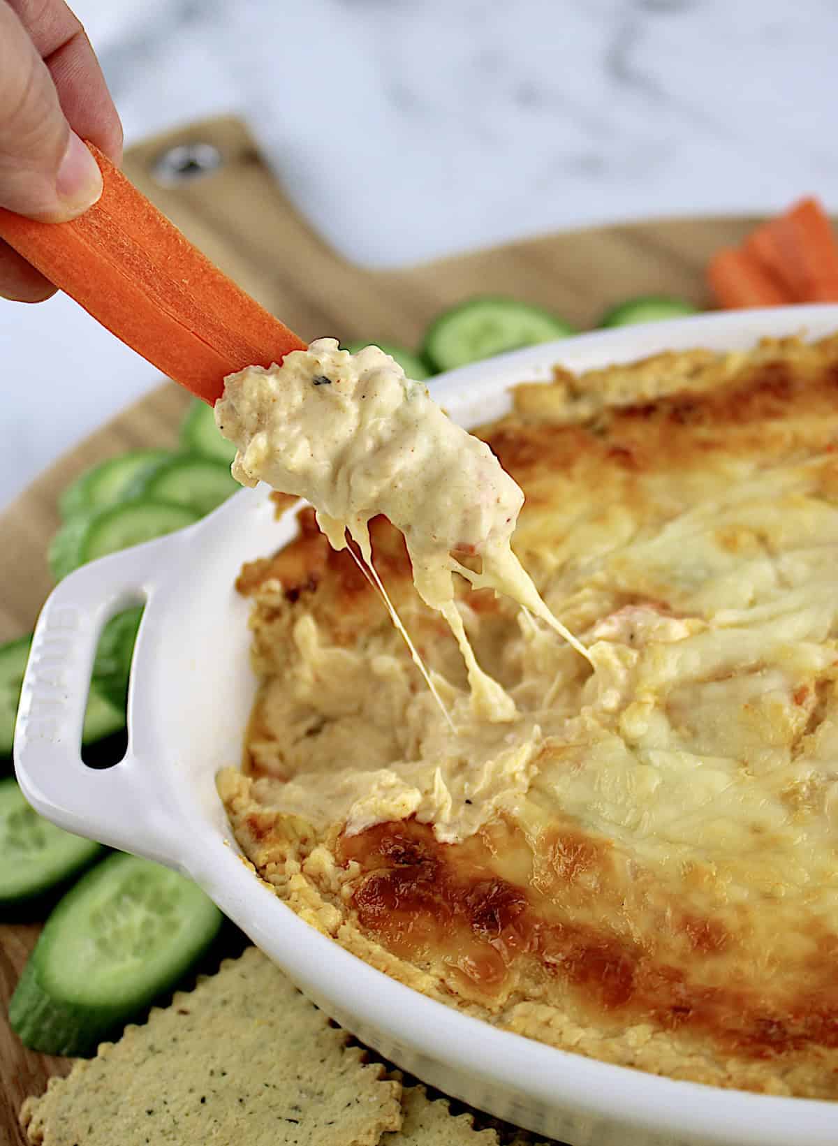 Hot Crab Dip being scooped by carrot stick with cucumbers in background