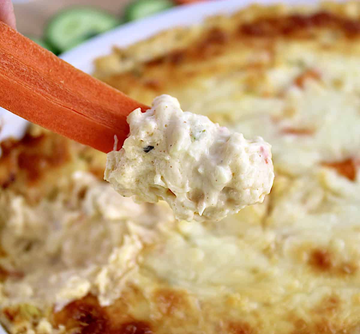 Hot Crab Dip being scooped by carrot stick with cucumbers in background