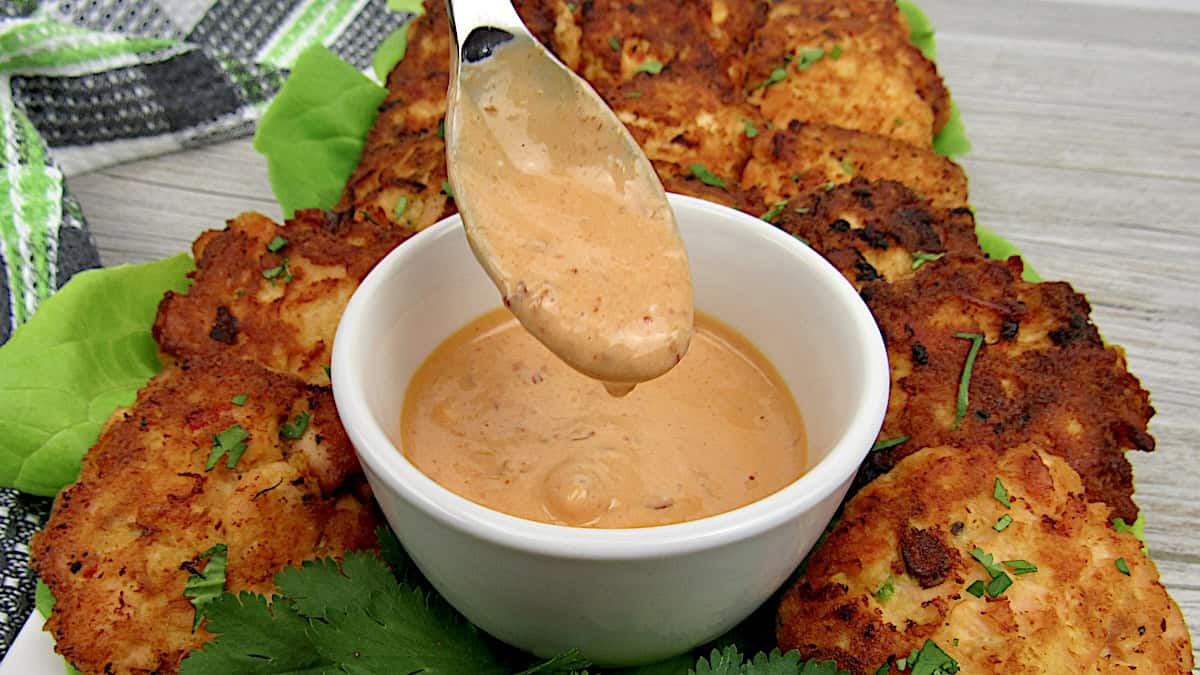 Keto Bang Bang Sauce dripping from spoon with salmon cakes in background