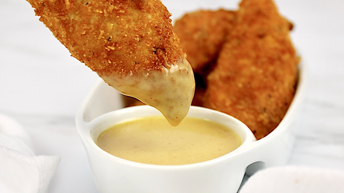 chicken tender being dipped into honey mustard