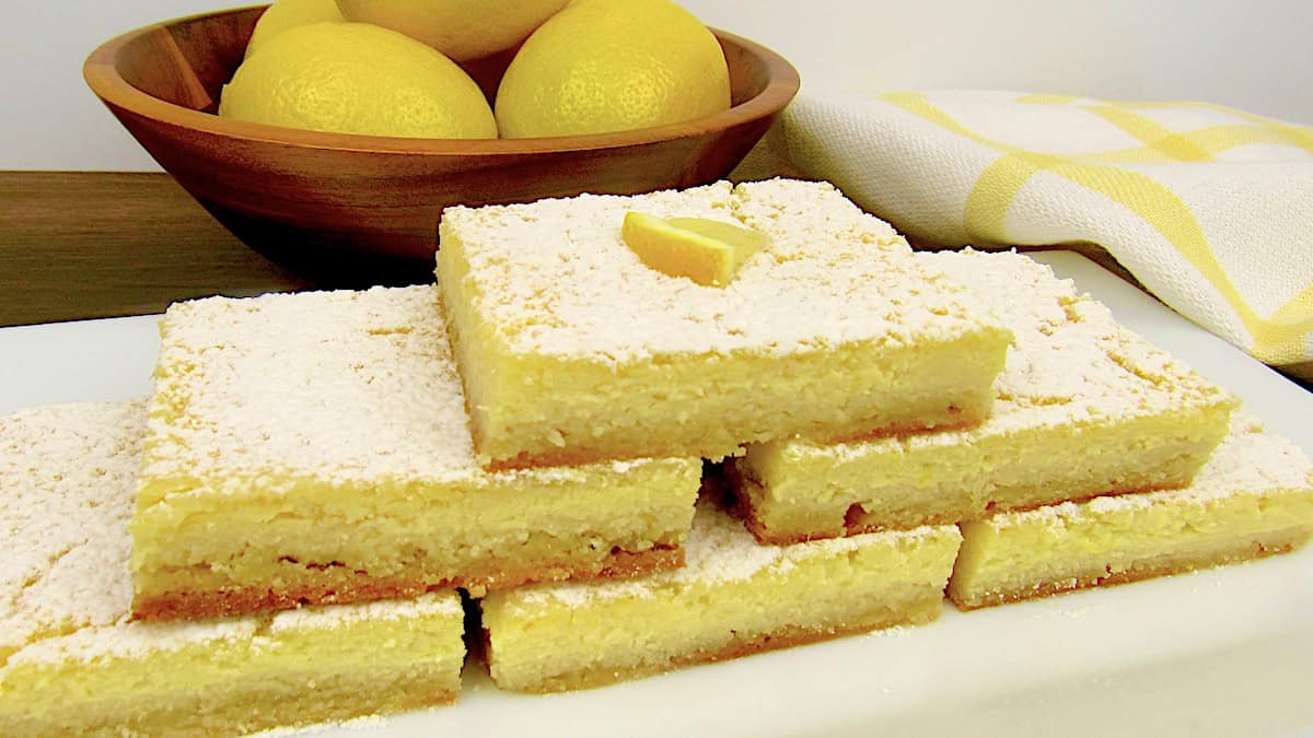 Keto Lemon Bars stacked up on white plate with lemons in background