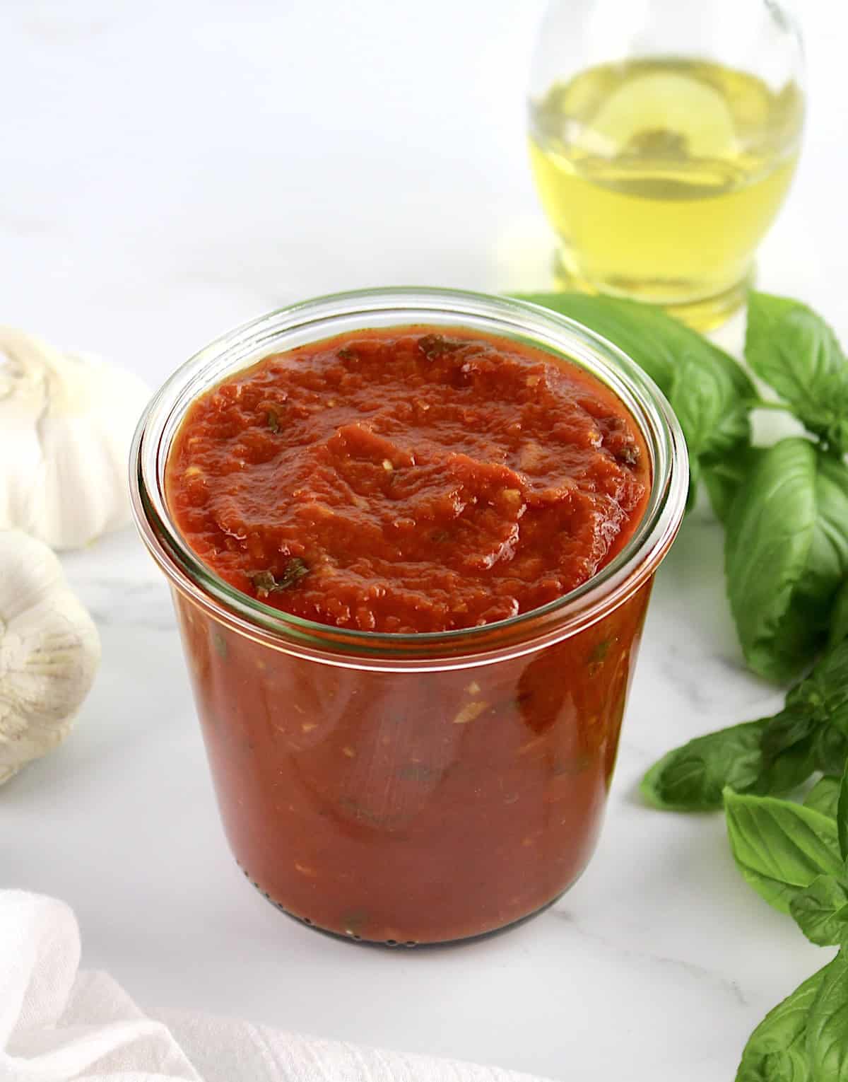 Keto Marinara Sauce in ope glass jar with basil and garlic in back