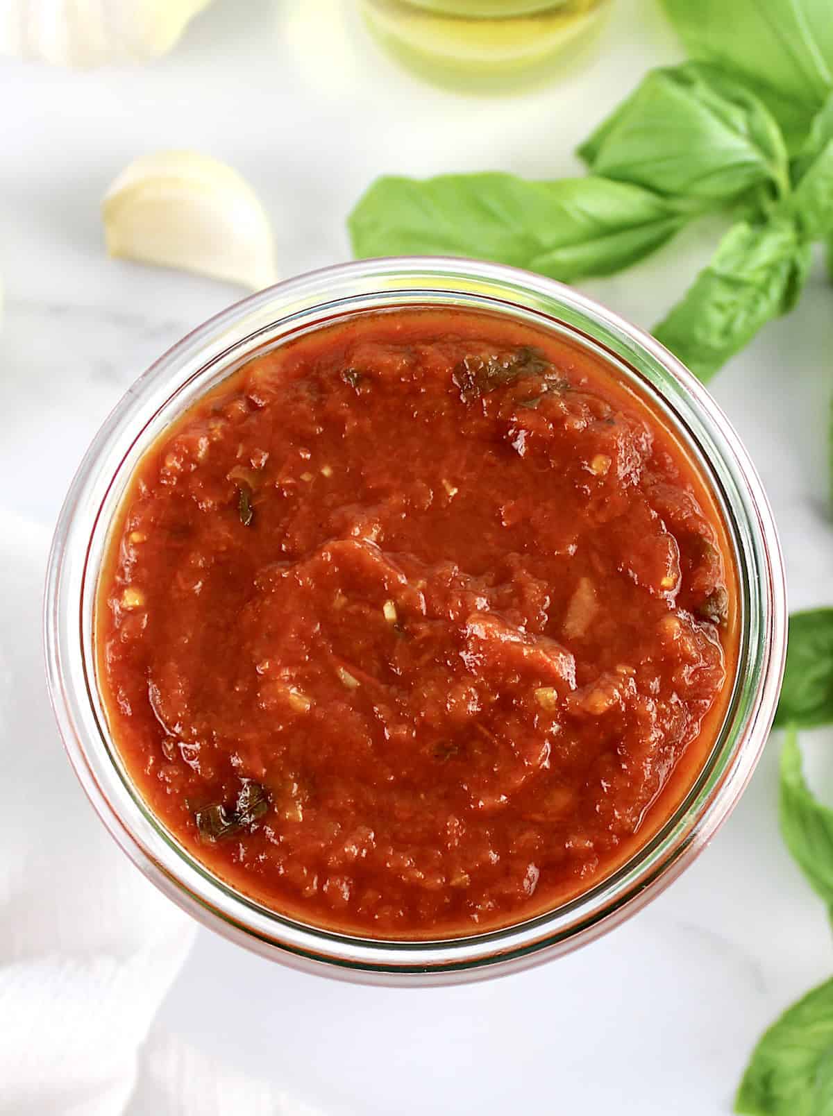 Keto Marinara Sauce in ope glass jar with basil and garlic in back