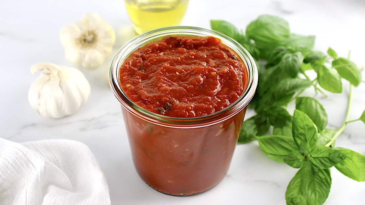 Keto Marinara Sauce in open glass jar with basil and garlic in back