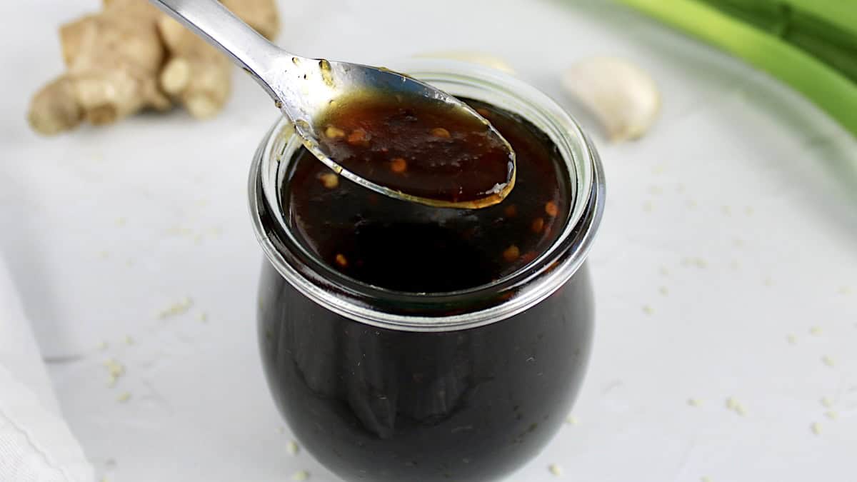 Keto Teriyaki Sauce being spooned from open jar with stir fry bowl in background