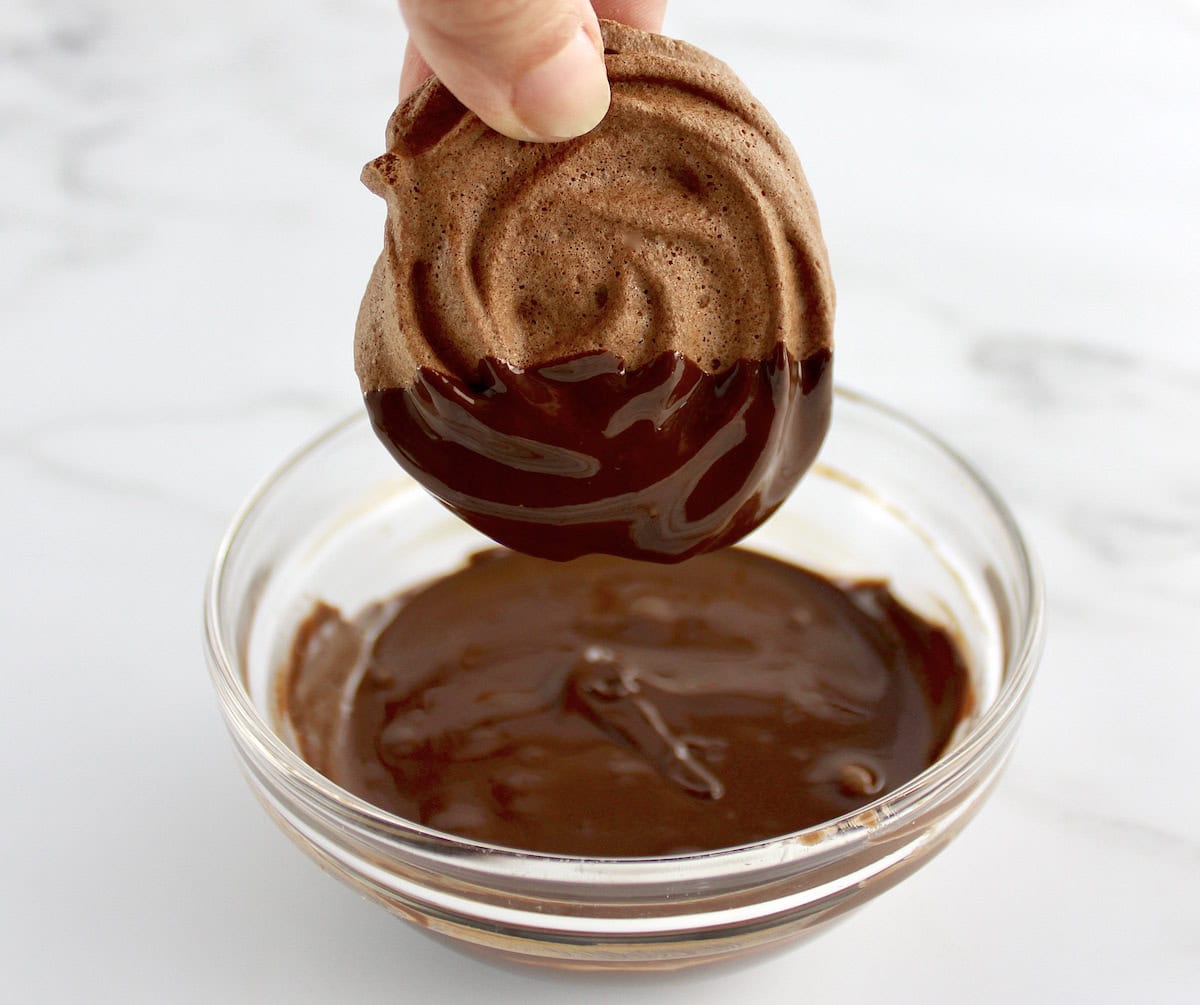 Mocha Meringue Cookie being dipped in melted chocolate in glass bowl