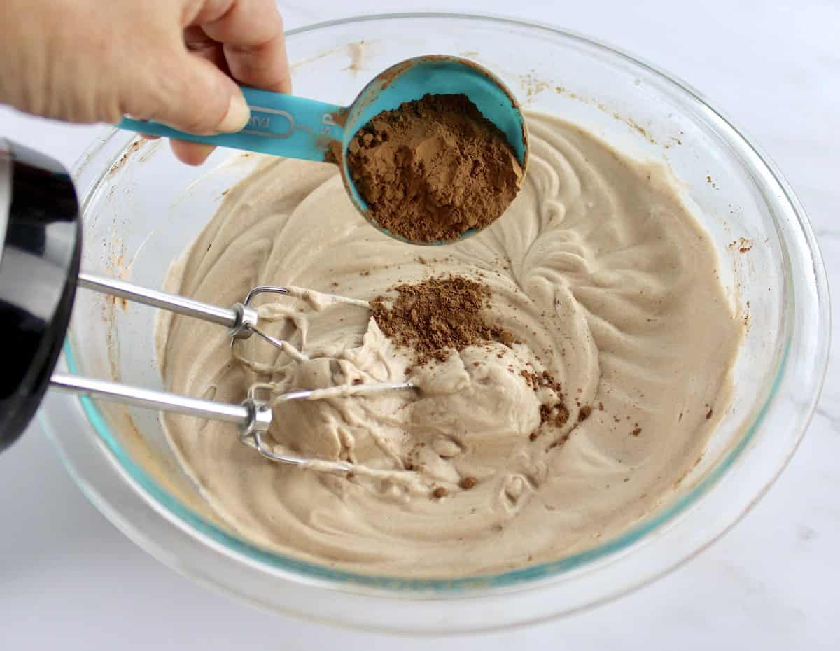 Mocha Meringue Cookie batter in glass bowl with cocoa powder being added