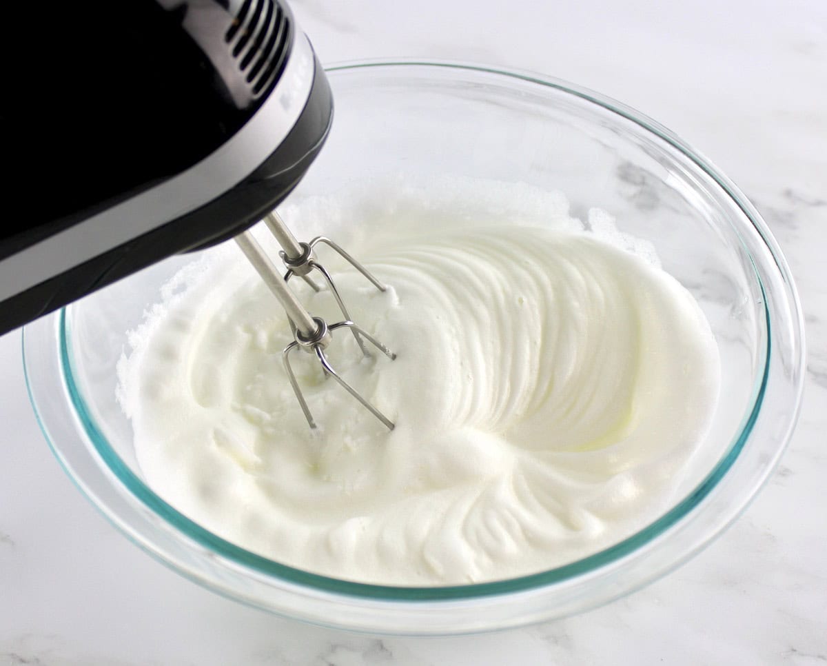 whipped egg whites in glass bowl with hand mixer