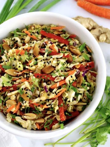 Peanut Ginger Slaw in white bowl with scallions carrots and ginger in background