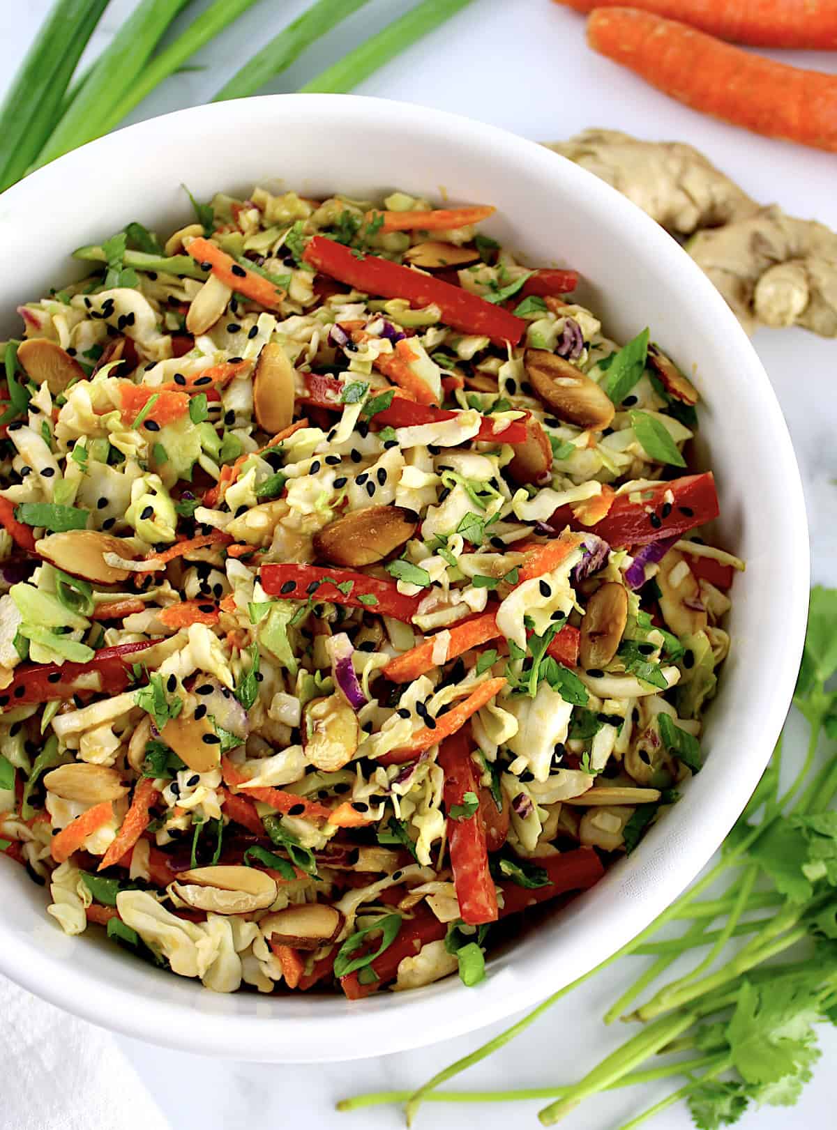 Peanut Ginger Slaw in white bowl with scallions carrots and ginger in background