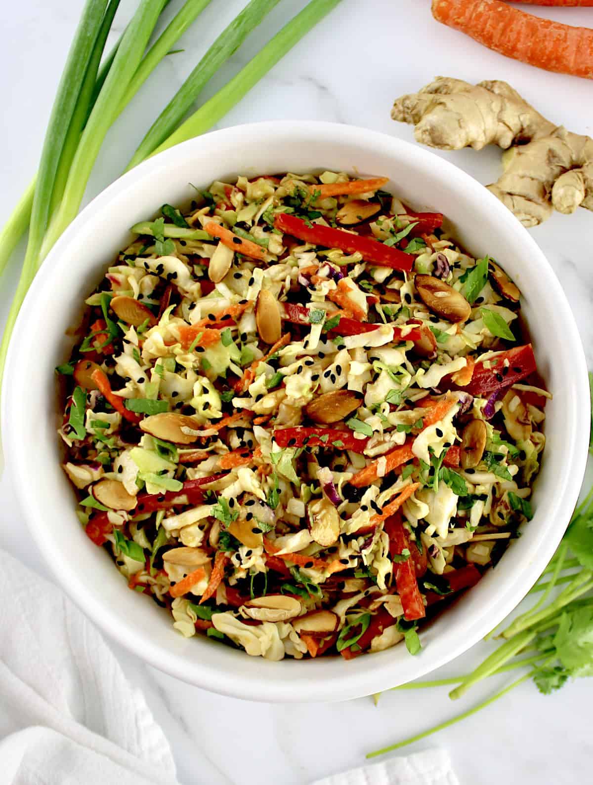 Peanut Ginger Slaw in white bowl with scallions carrots and ginger in background