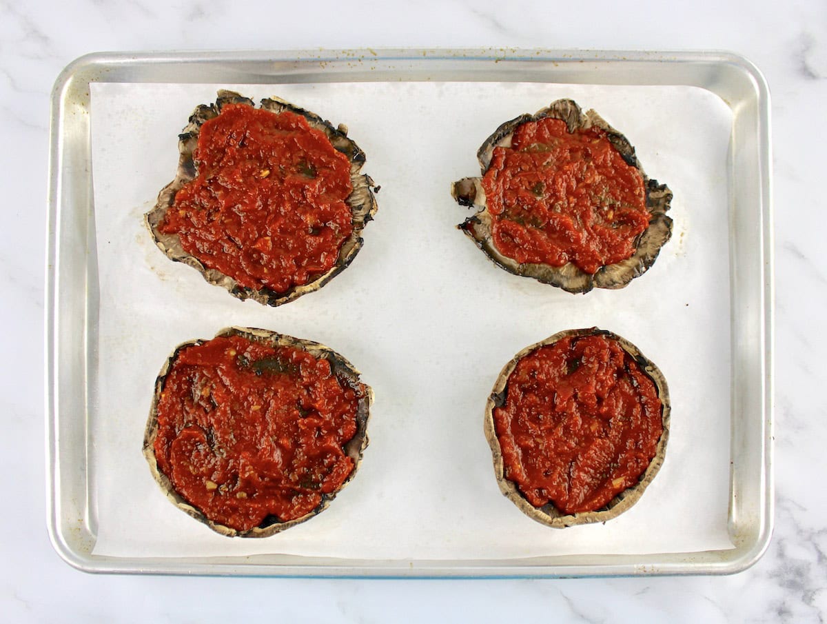 4 portobello mushroom caps with marinara sauce on parchment lined baking sheet