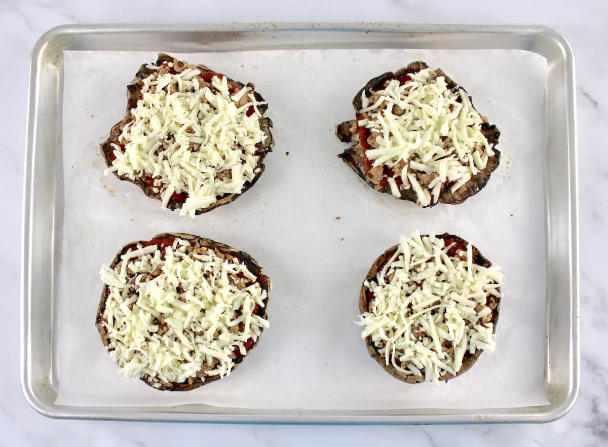 4 portobello mushroom caps with marinara sauce and sausage and shredded cheese parchment lined baking sheet