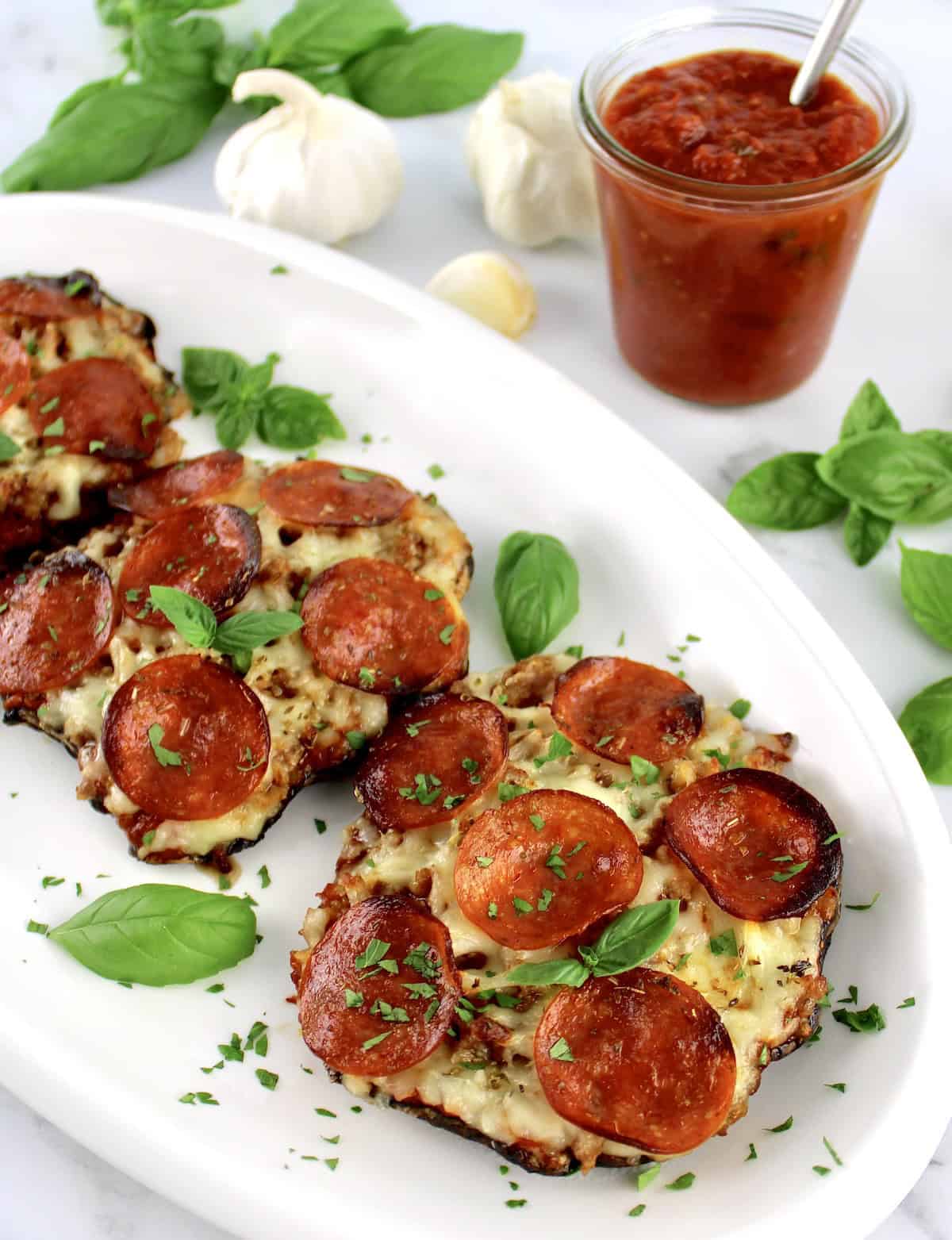 3 Portobello Mushroom Mini Pizzas on white plate with fresh basil garish and marinara sauce in back