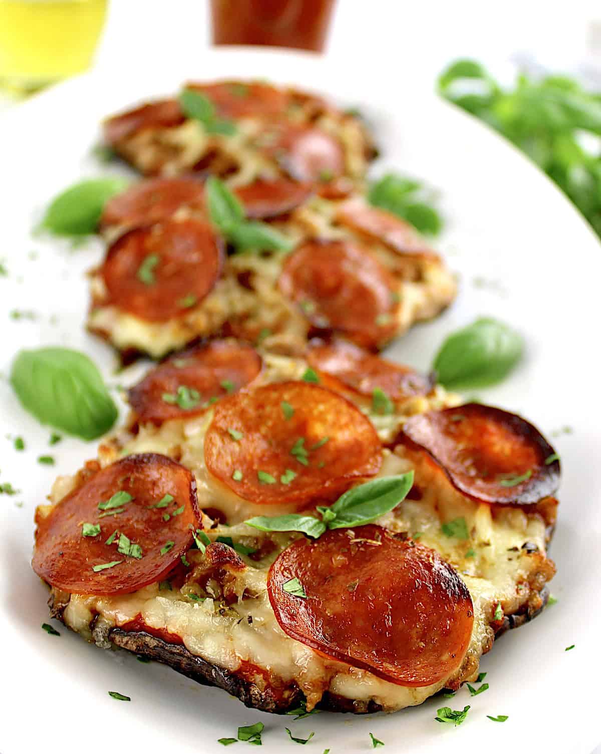 closeup of 3 Portobello Mushroom Mini Pizzas on white plate with fresh basil leaves