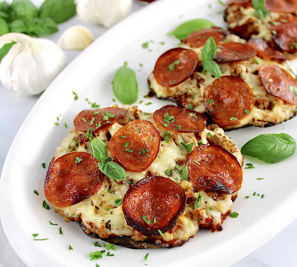 closeup of Portobello Mushroom Mini Pizzas on white plate with basil garnish