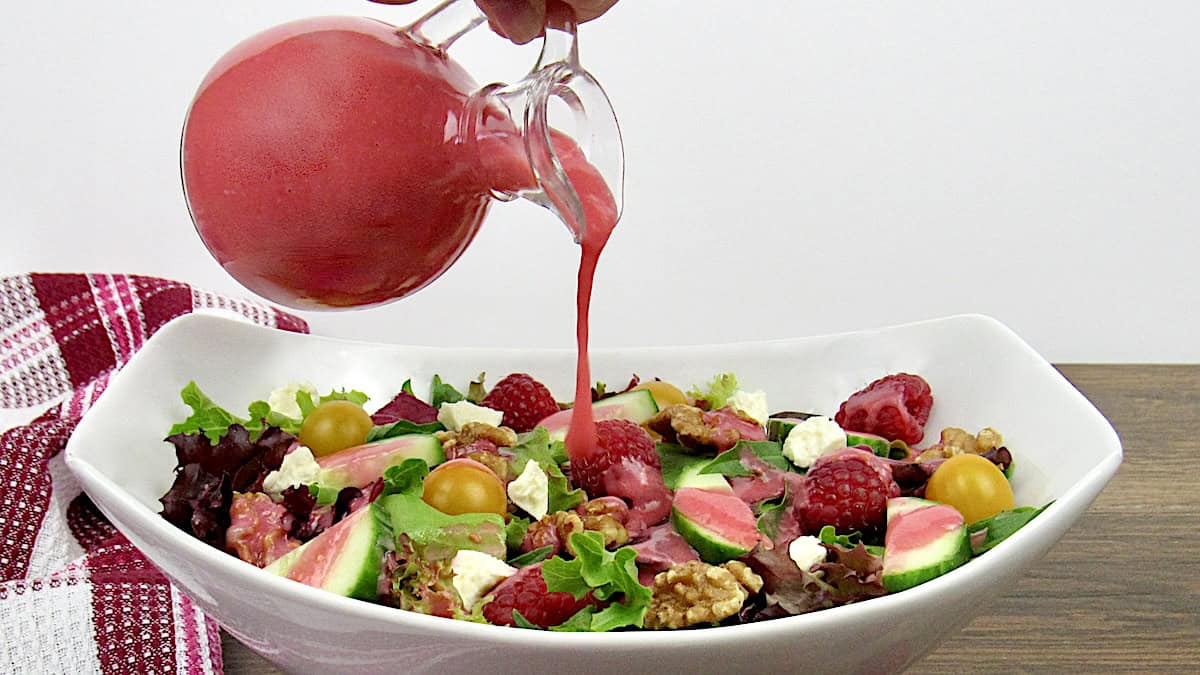 Raspberry Vinaigrette being poured over salad in white bowl