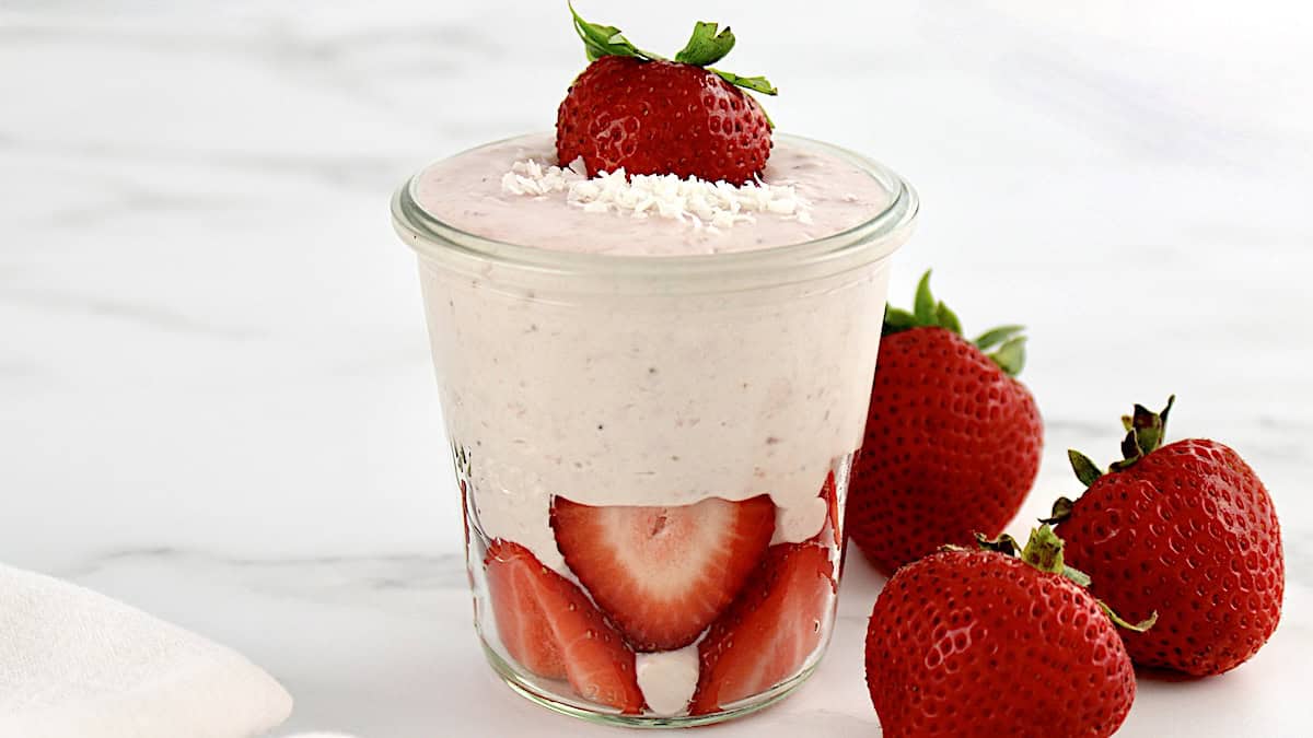 side view of Strawberry Coconut Cream Mousse in glass jar with sliced strawberries and shredded coconut