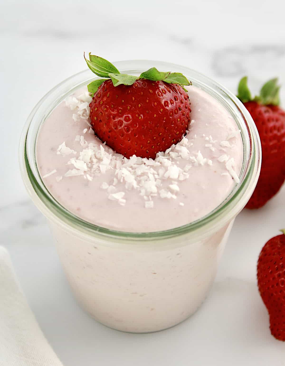 overhead view of Strawberry Coconut Cream Mousse in glass jar with strawberry and shredded coconut on top