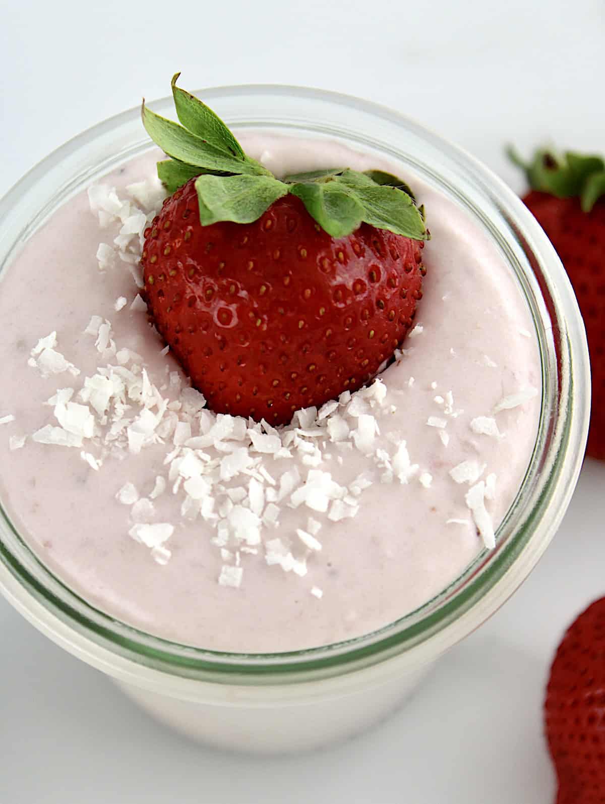 overhead closeup of Strawberry Coconut Cream Mousse in glass jar with whole strawberry and shredded coconut on top