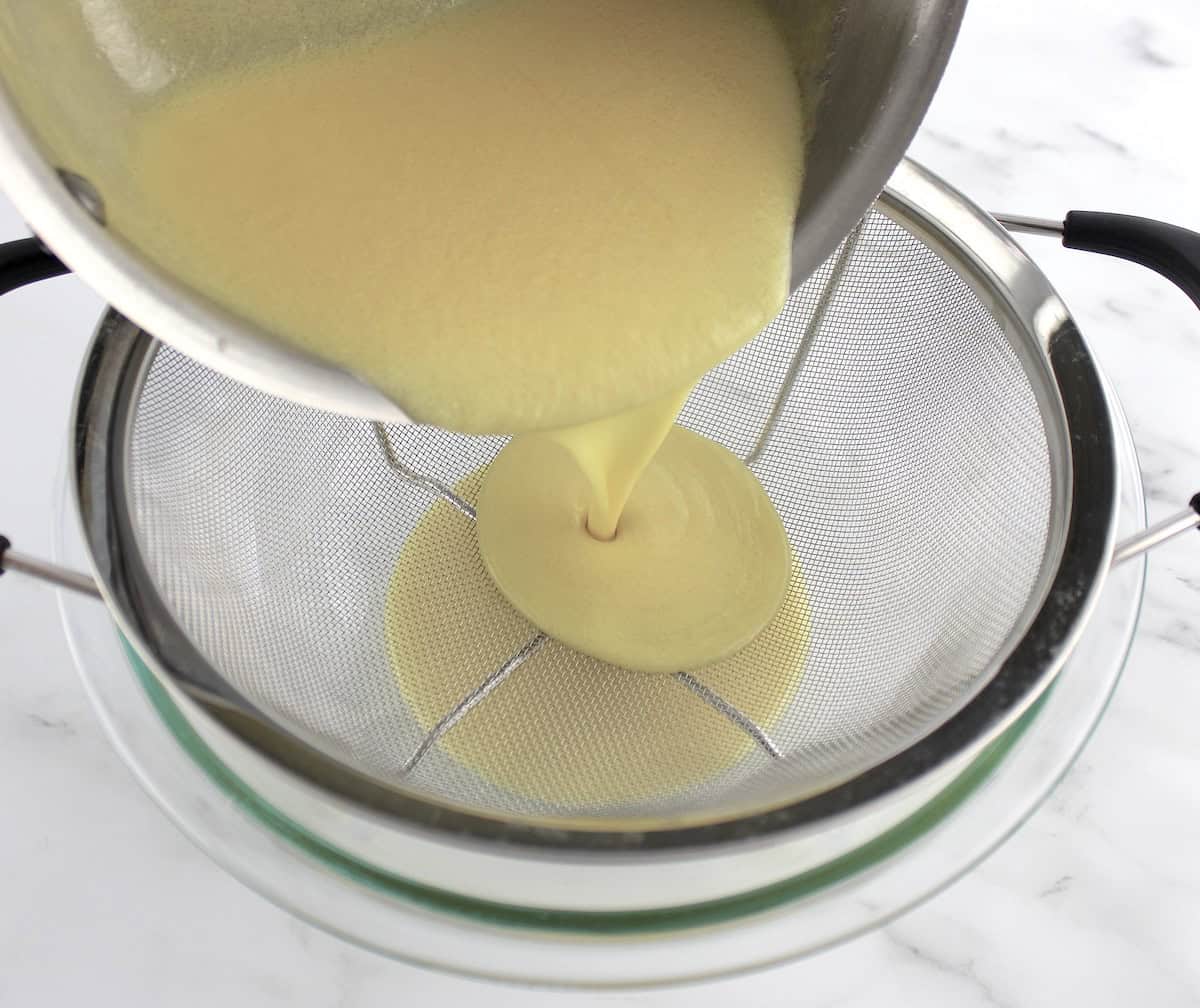 ice cream custard being poured from saucepan through fine mesh sieve