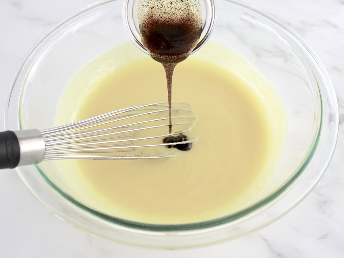 vanilla bean paste being whisked into ice cream custard in glass bowl