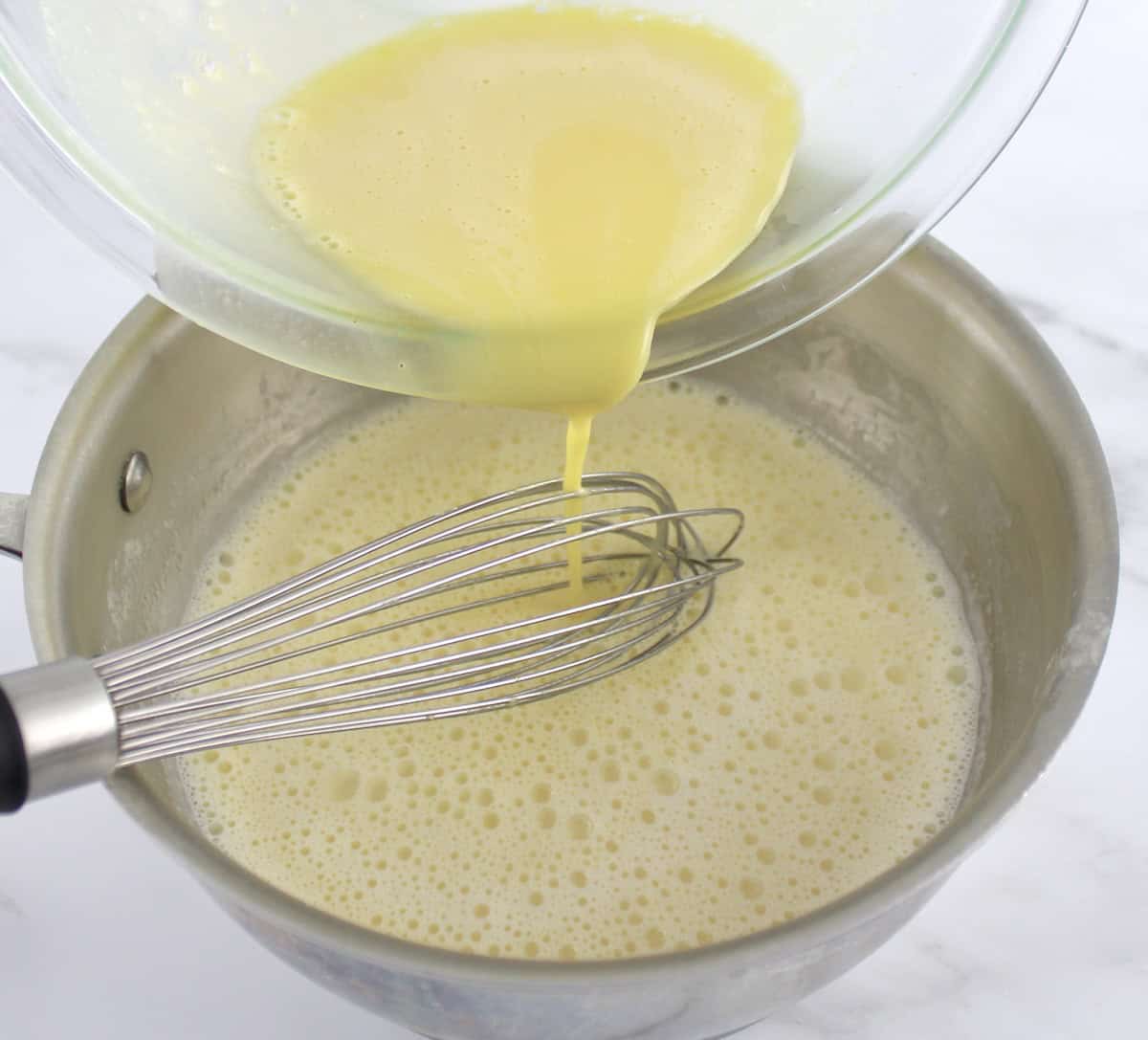 egg yolk mixture being ladled into saucepan with cream and whisk