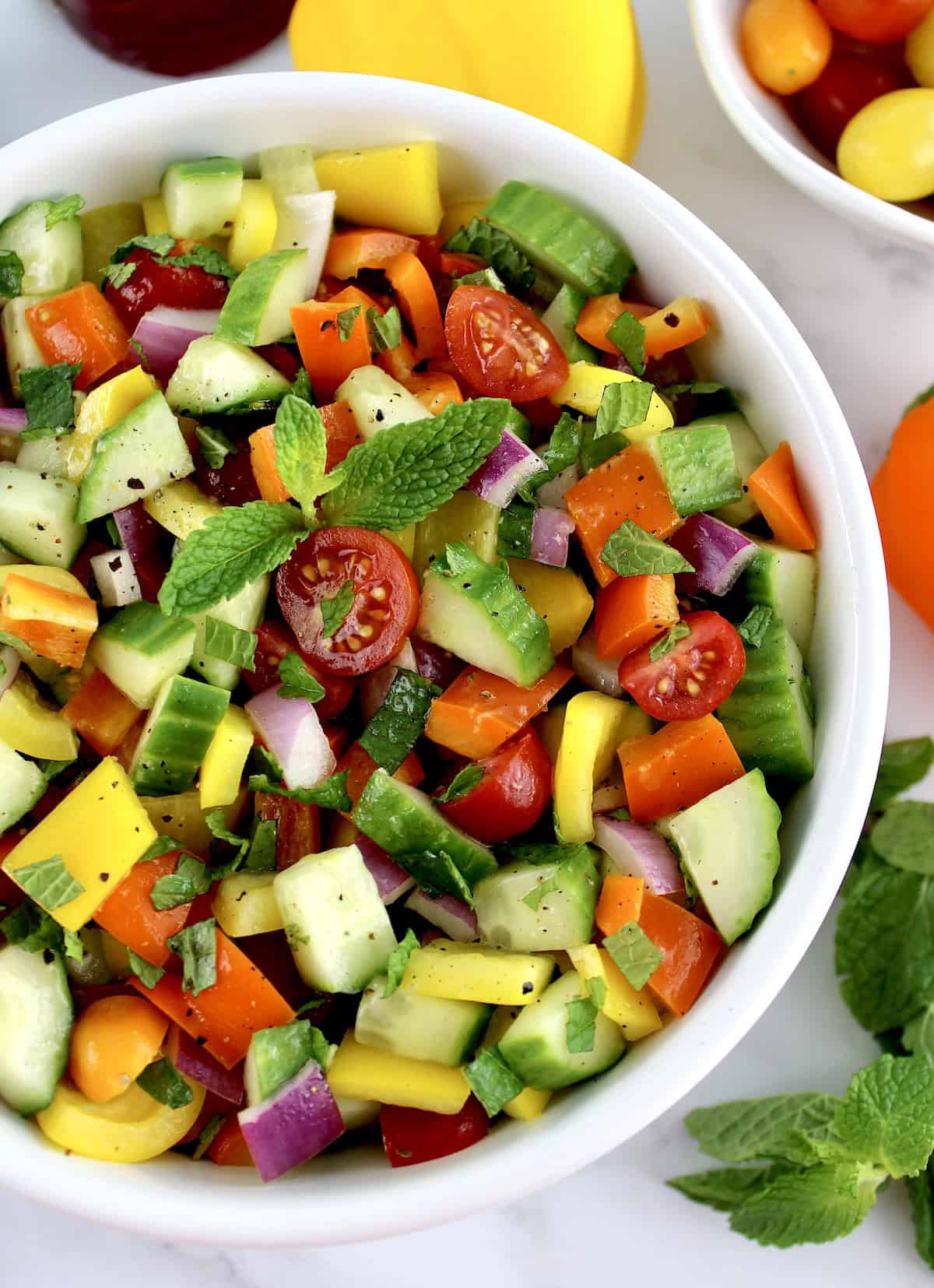 Israeli Salad in white bowl with veggies in back