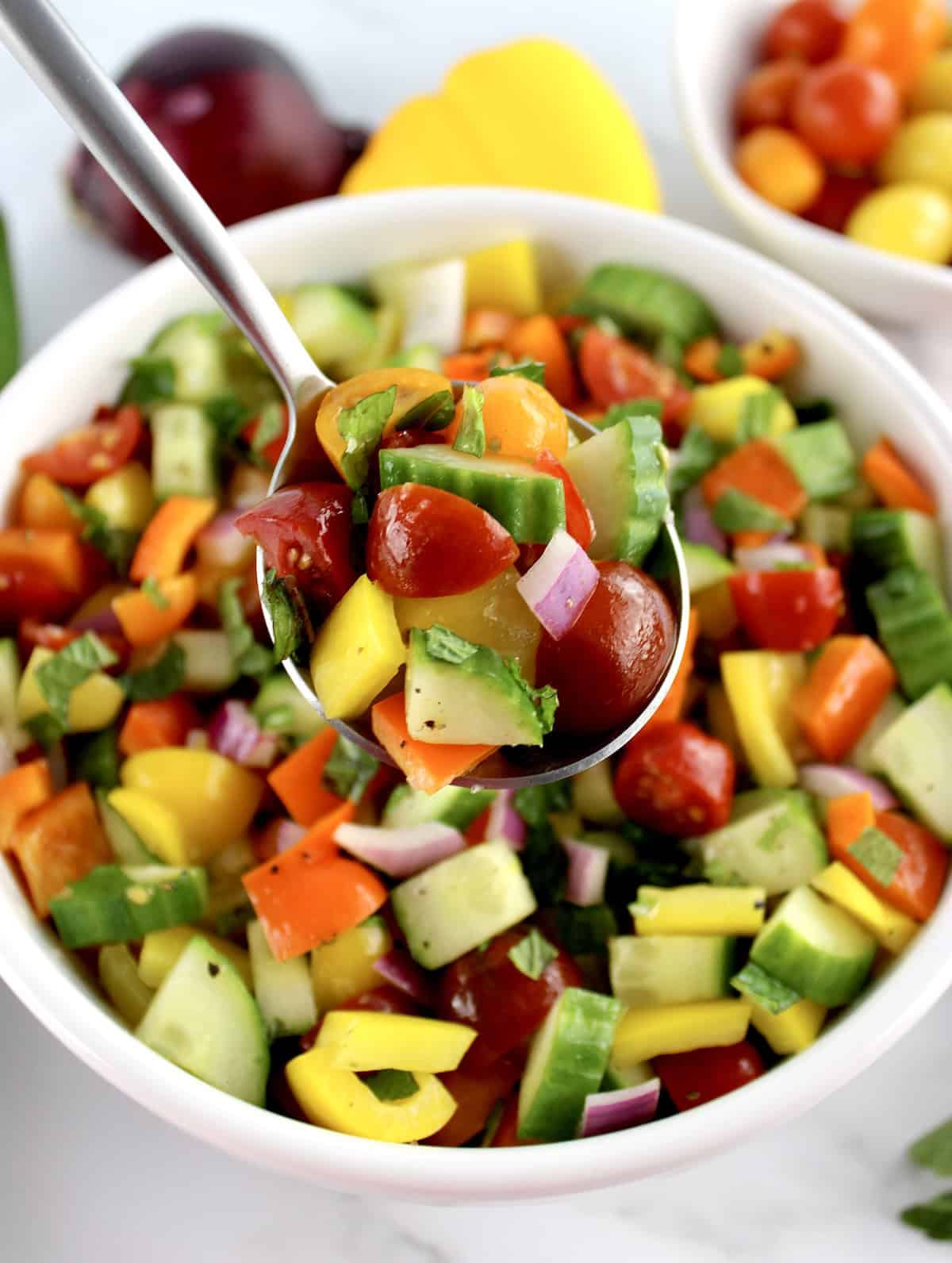 Israeli Salad in spoon held up over salad in white bowl