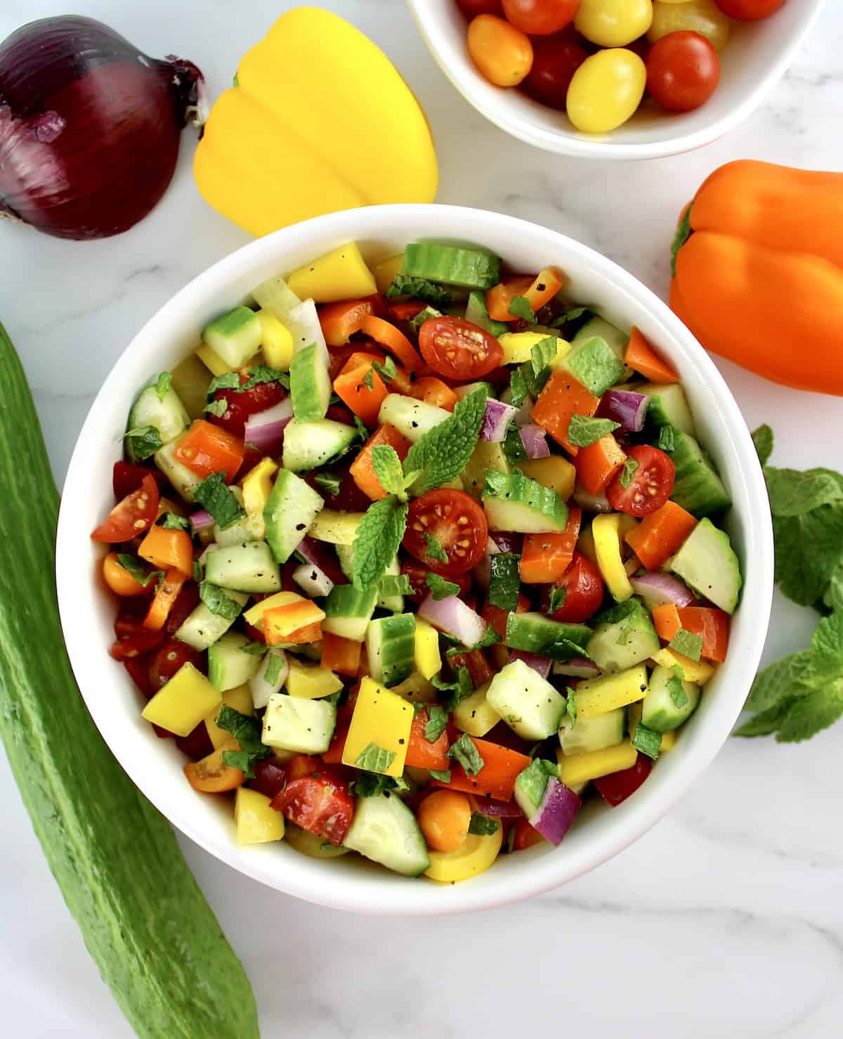 overhead view of Israeli Salad in white bowl with fresh veggies in background