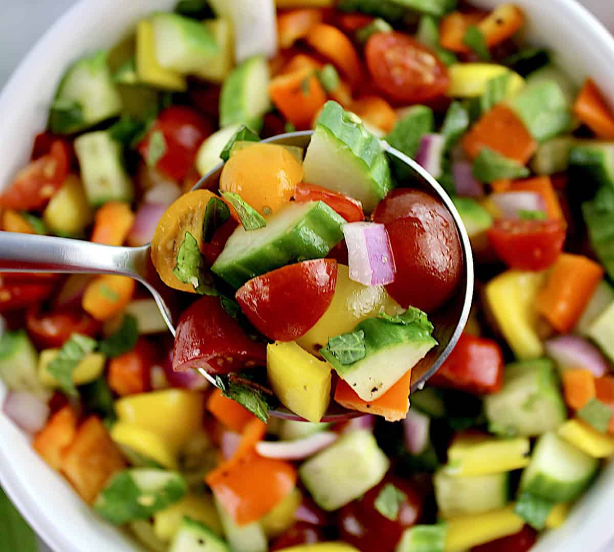 Israeli Salad in silver spoon held up over salad in white bowl