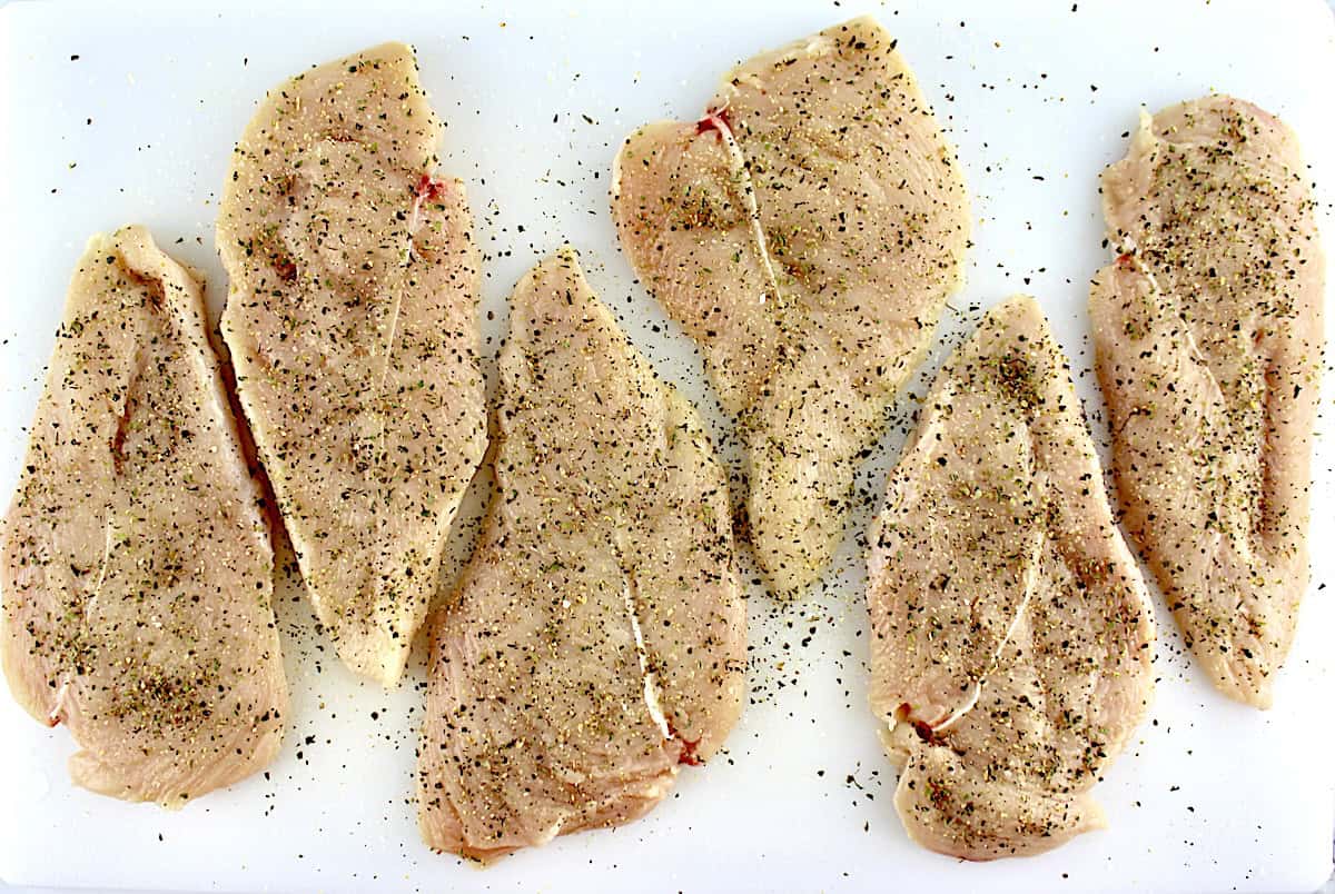 6 raw chicken breasts with spices on top on white cutting board