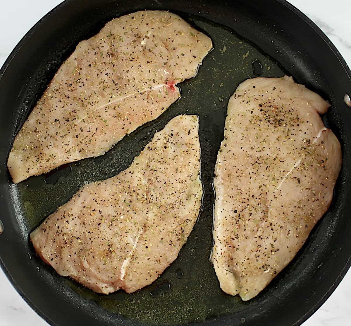 3 raw chicken breasts with spices in skillet