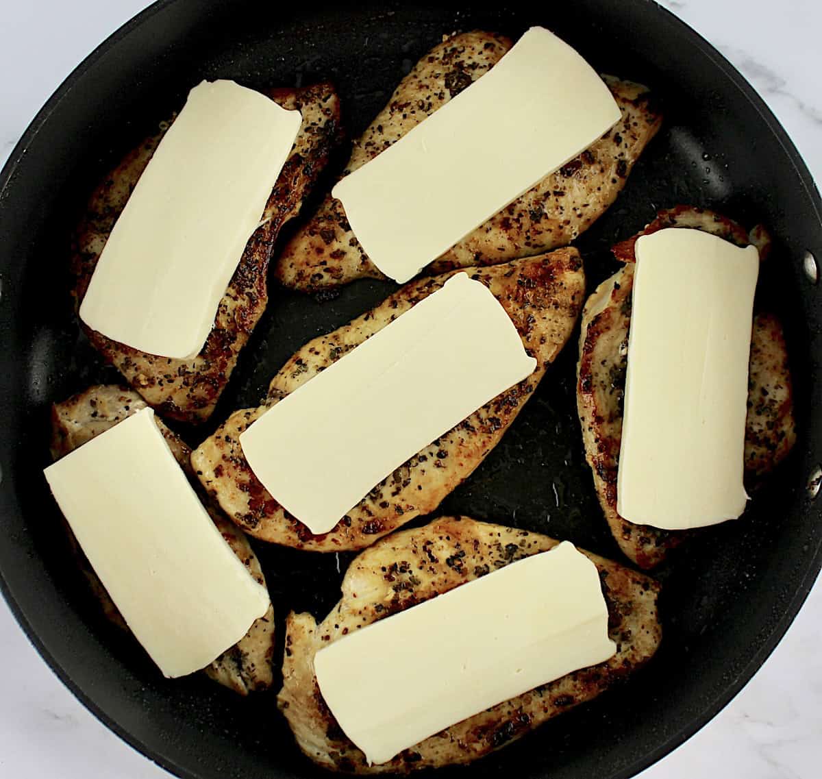 6 chicken breasts in skillet with mozzarella slices on top