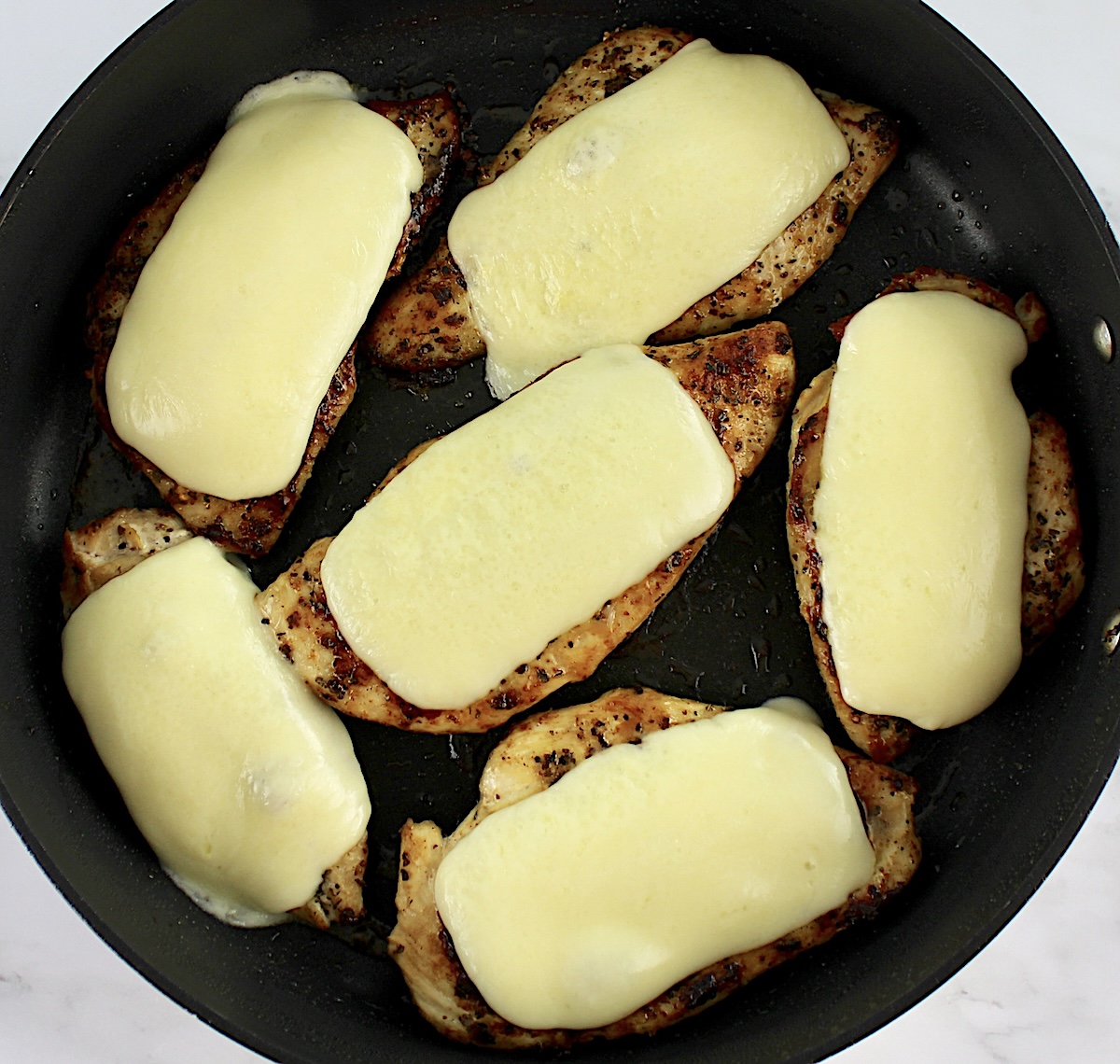 6 chicken breasts in skillet with melted mozzarella slices on top