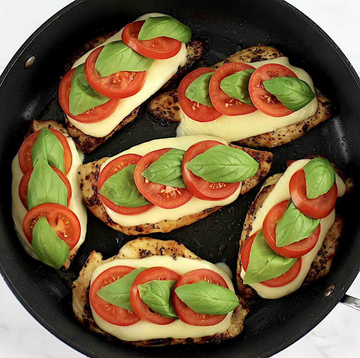 Chicken Caprese in skillet with slices of tomatoes and fresh basil leaves on top