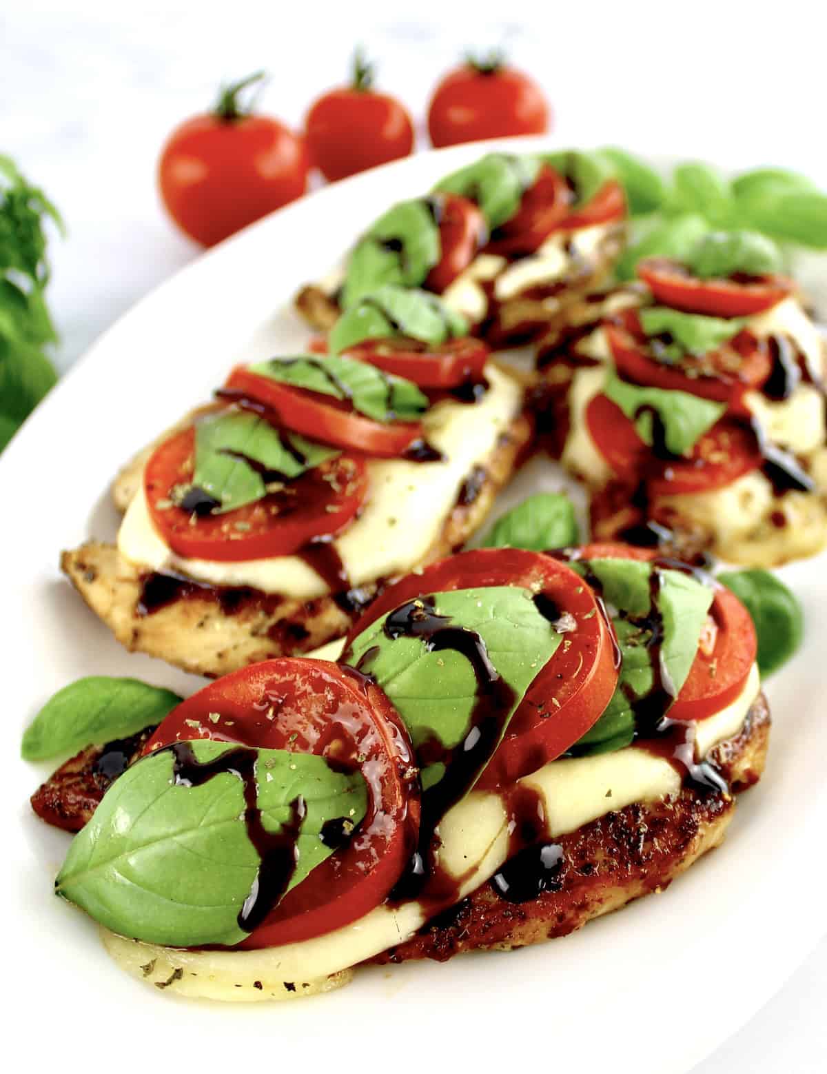 closeup of Chicken Caprese on white oval platter with balsamic glaze drizzled on top