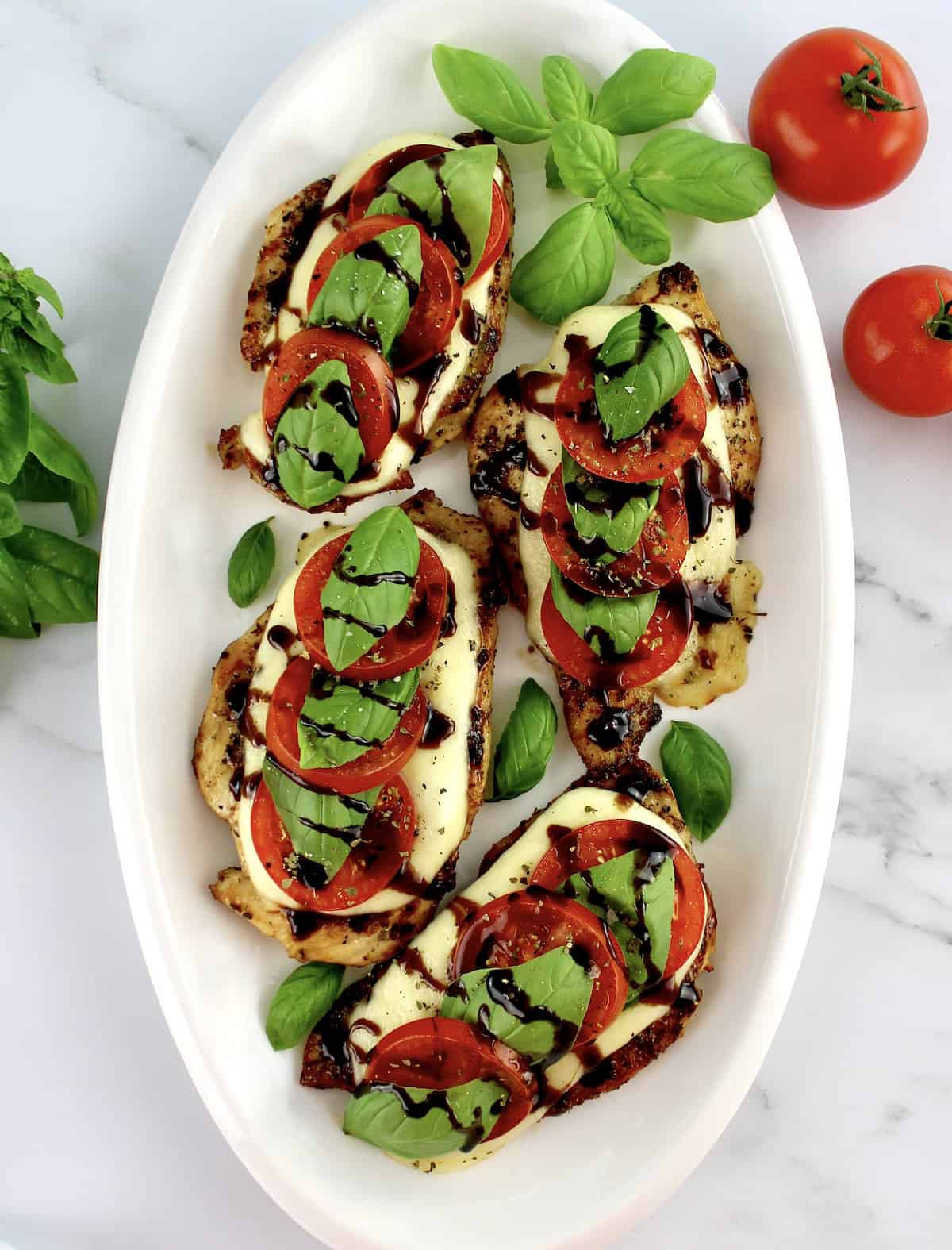 overhead view of Chicken Caprese on white oval platter with balsamic glaze drizzled on top