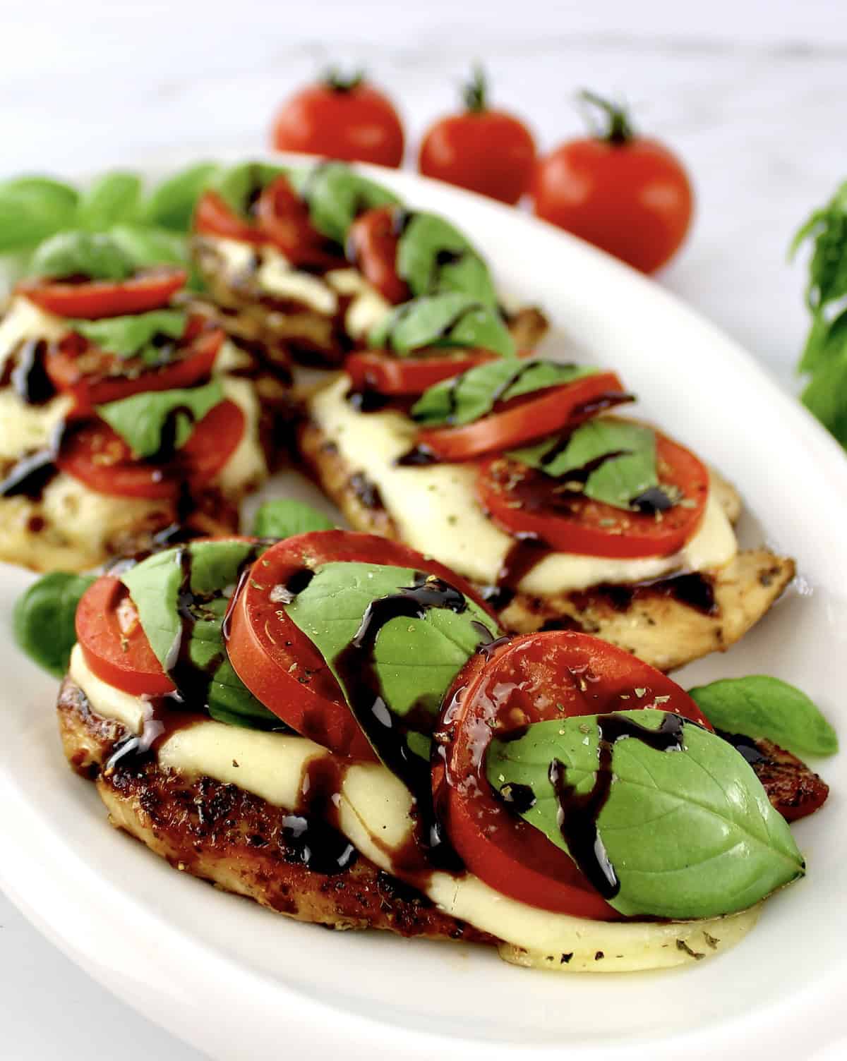 closeup of Chicken Caprese on white oval platter with balsamic glaze drizzled on top