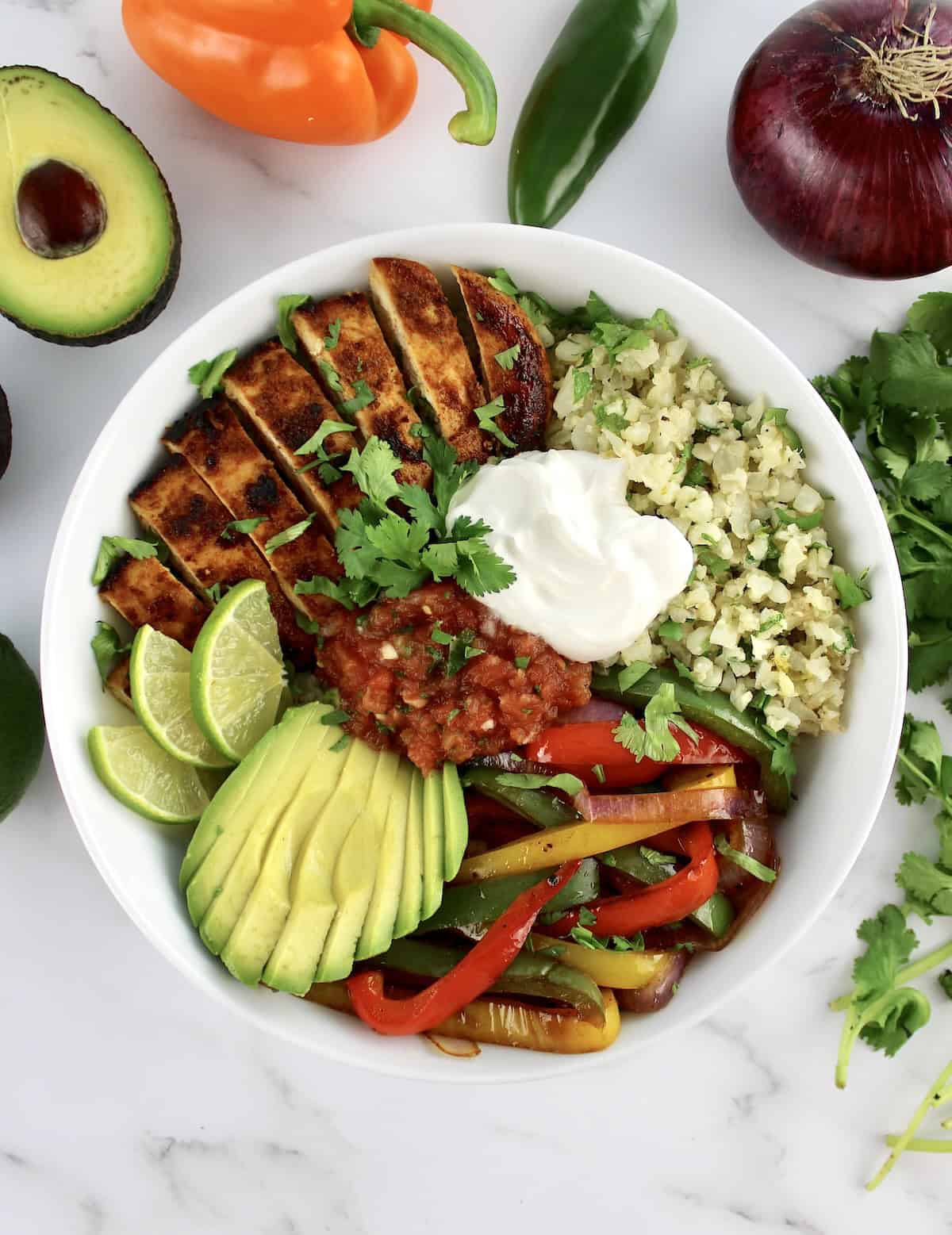 overhead view of Chicken Fajita Bowl with salsa and sour cream with veggies in background