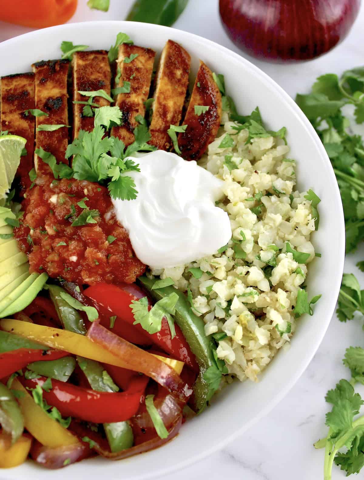 overhead view of Chicken Fajita Bowl with salsa and sour cream and veggies in background