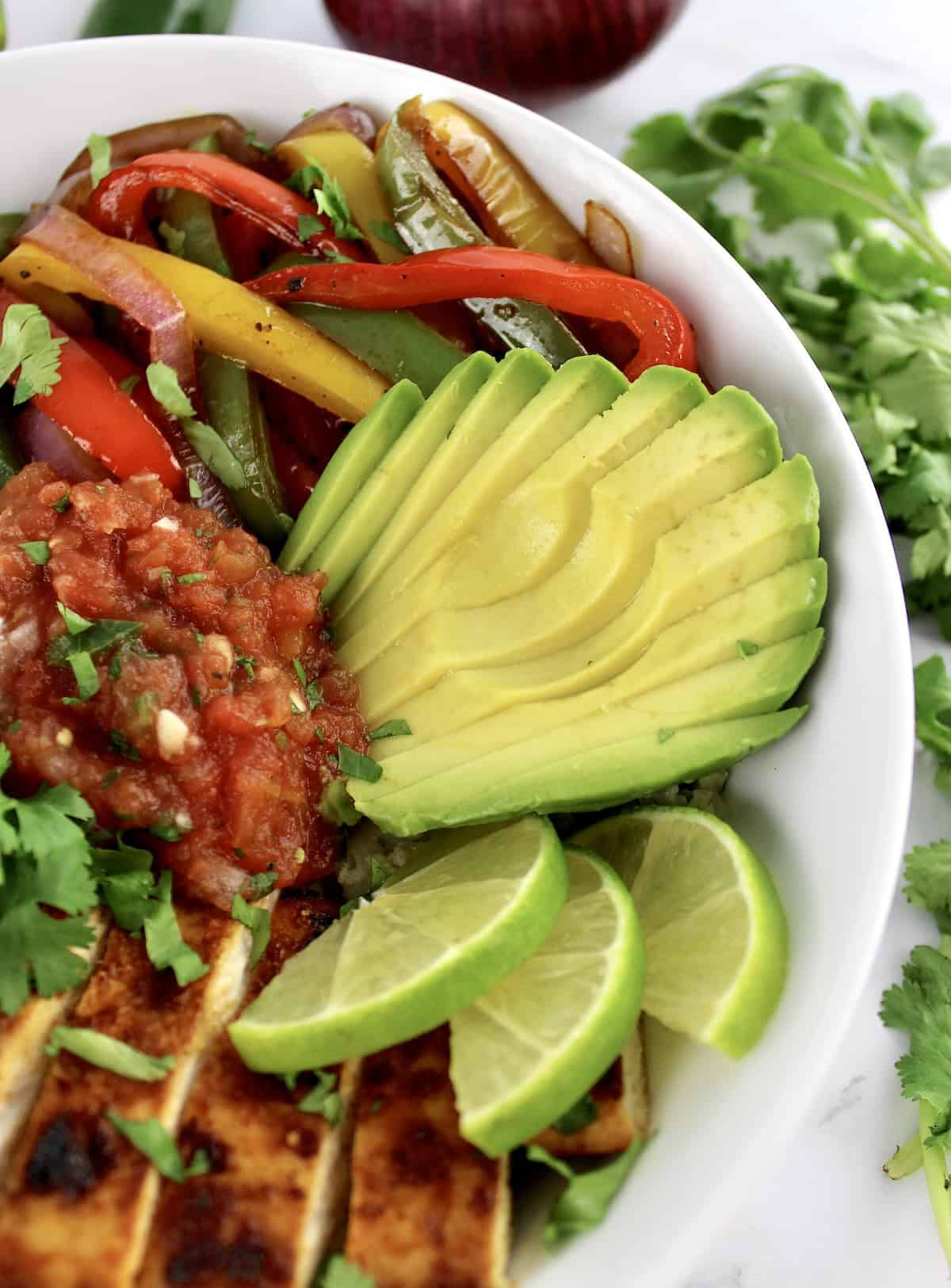 closeup of Chicken Fajita Bowl with sliced avocado salsa peppers and lime slices