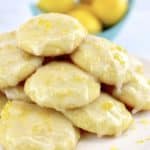 Lemon Ricotta Cookies stacked up on white plate with lemons in background