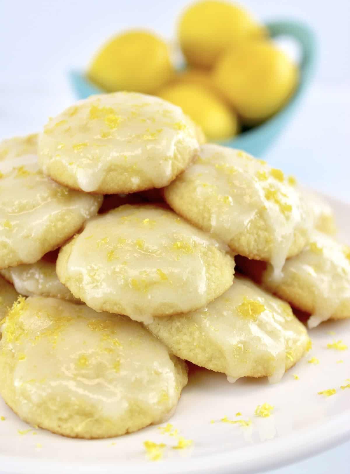 Lemon Ricotta Cookies stacked up on white plate with lemons in background