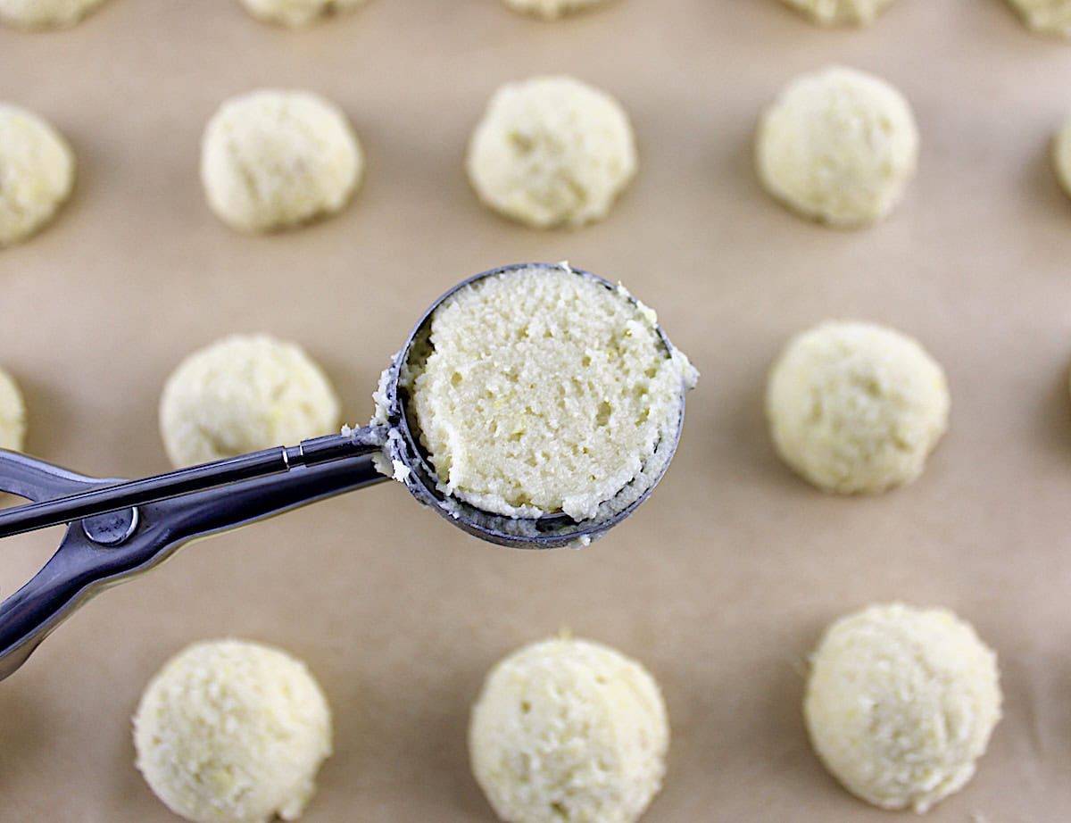 Lemon Ricotta Cookie dough in cookie scooper with dough on parchment paper in back