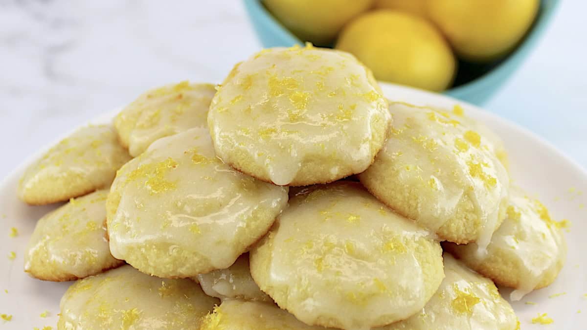 Lemon Ricotta Cookies stacked up on white plate with lemons in back