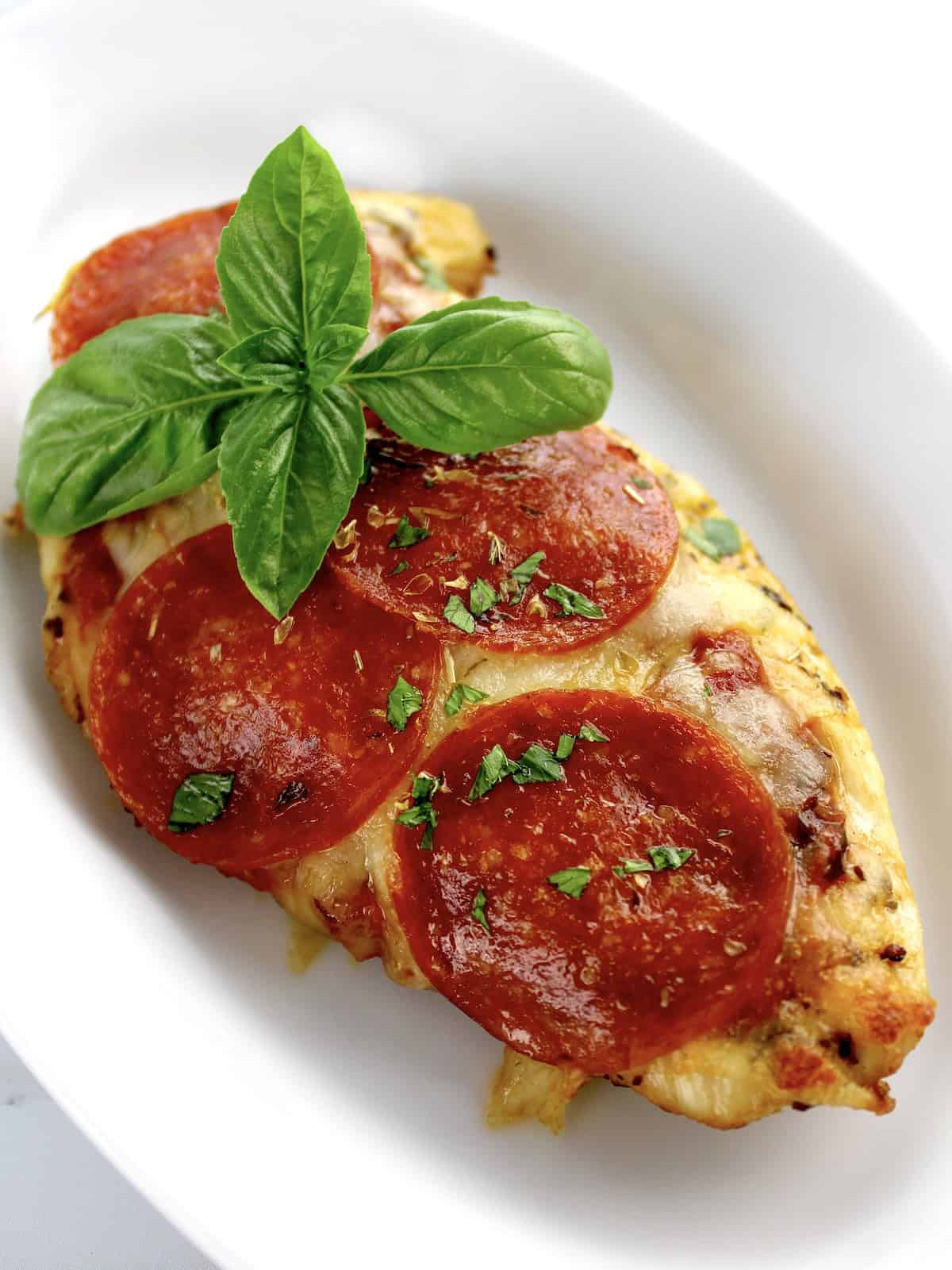 piece of Pizza Chicken on white oval plate with fresh basil garnish