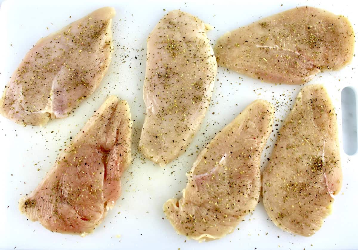 6 pieces of raw chicken on white cutting board with spices on top