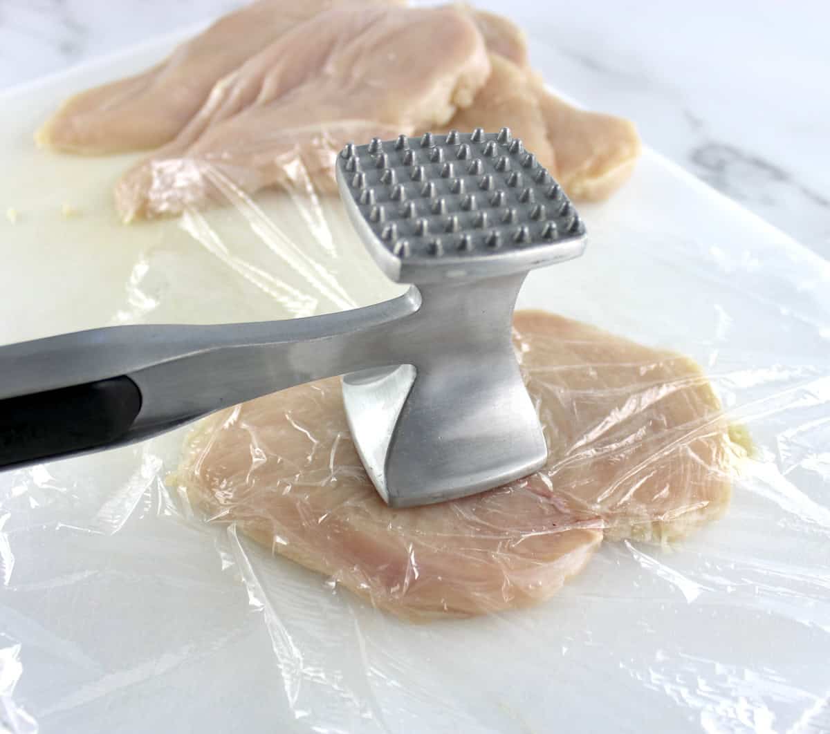 chicken breast on white cutting board with meat tenderizer hitting it